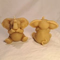 Front and back view of two laughing elephant-shaped candles on a light background